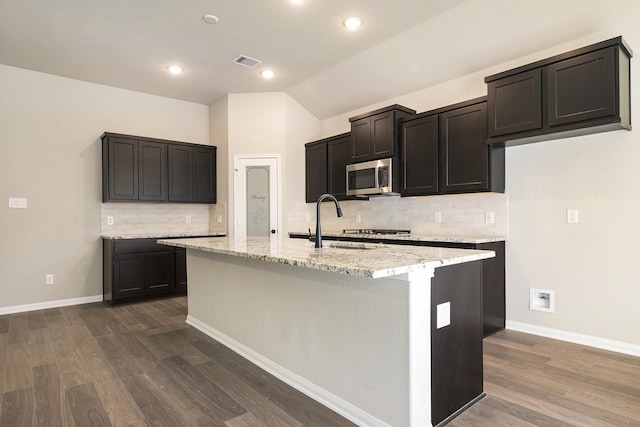 kitchen featuring light stone counters, dark wood-type flooring, a kitchen island with sink, and vaulted ceiling