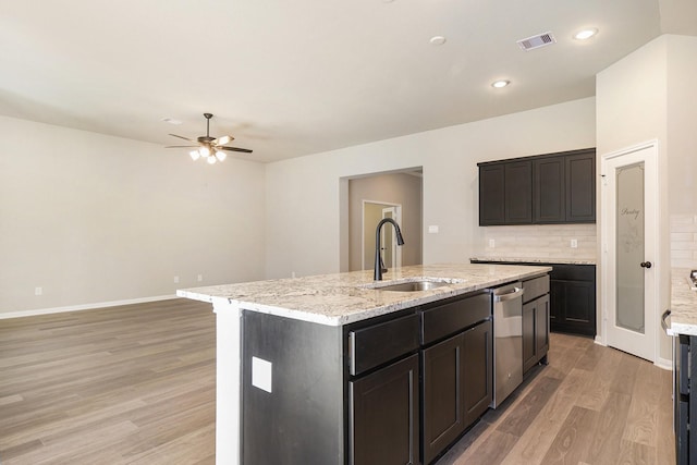 kitchen with stainless steel dishwasher, decorative backsplash, sink, and a kitchen island with sink