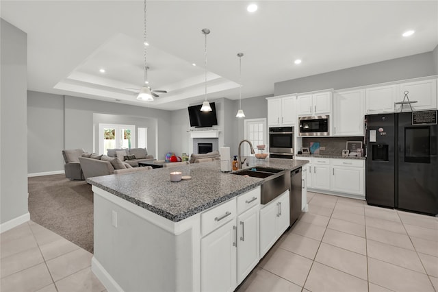 kitchen with appliances with stainless steel finishes, a tray ceiling, white cabinetry, light carpet, and a kitchen island with sink