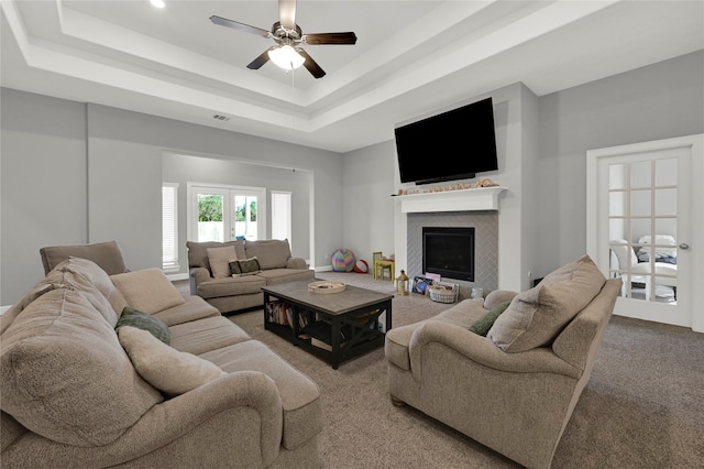 carpeted living room with ceiling fan and a raised ceiling