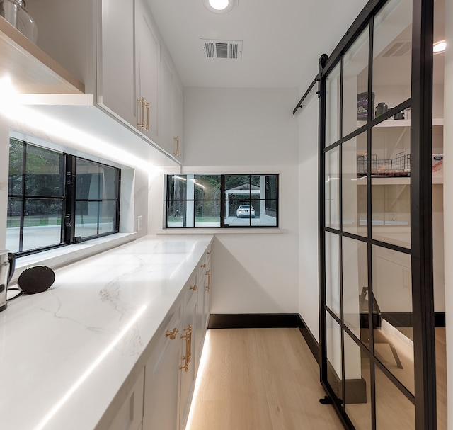 interior space with white cabinetry, light stone counters, light hardwood / wood-style flooring, and a barn door