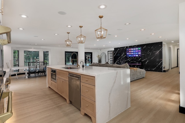 kitchen with light stone countertops, a kitchen island with sink, hanging light fixtures, and light wood-type flooring