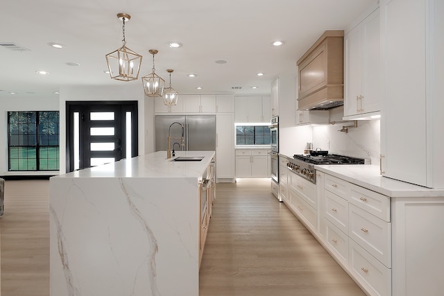 kitchen featuring a spacious island, sink, pendant lighting, light wood-type flooring, and white cabinets