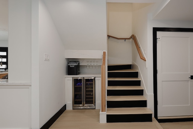 stairs with bar area, wood-type flooring, and beverage cooler