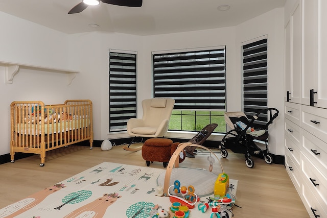 bedroom featuring light hardwood / wood-style flooring, a crib, and ceiling fan