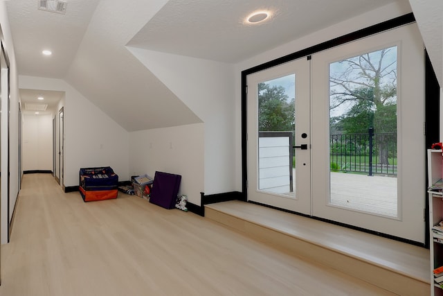 additional living space with french doors, light hardwood / wood-style floors, a textured ceiling, and lofted ceiling