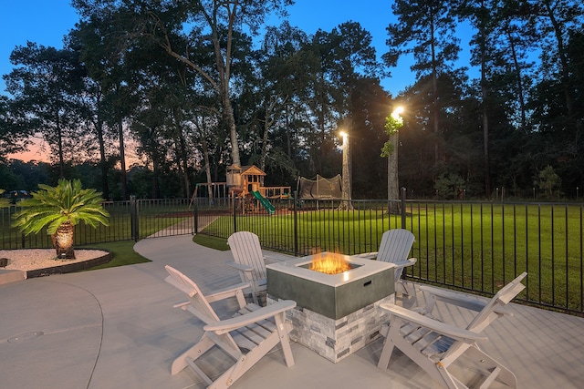 patio terrace at dusk with a yard, an outdoor fire pit, and a playground