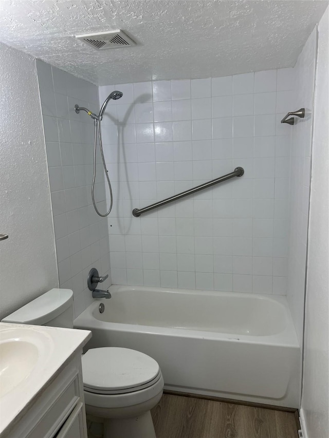 full bathroom with hardwood / wood-style floors, vanity, tiled shower / bath, toilet, and a textured ceiling