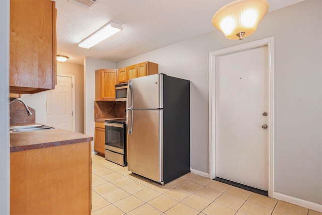 kitchen featuring sink, a textured ceiling, stainless steel appliances, light tile patterned floors, and light brown cabinets