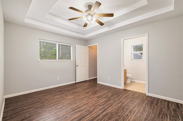 unfurnished bedroom featuring dark wood-type flooring, ceiling fan, ensuite bathroom, and a raised ceiling