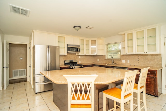 kitchen featuring a kitchen breakfast bar, sink, light tile patterned floors, appliances with stainless steel finishes, and a kitchen island