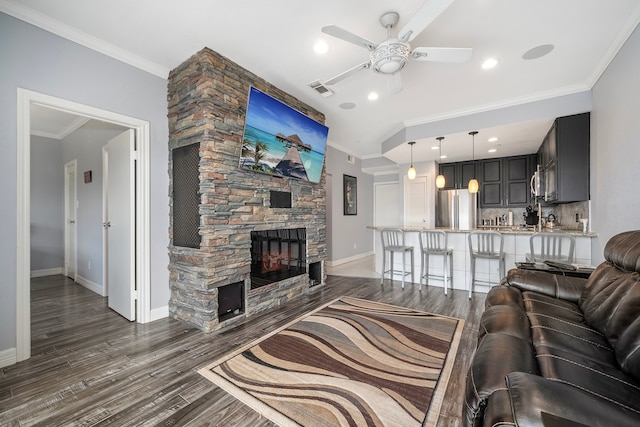 living room with dark hardwood / wood-style flooring, a stone fireplace, ceiling fan, and ornamental molding