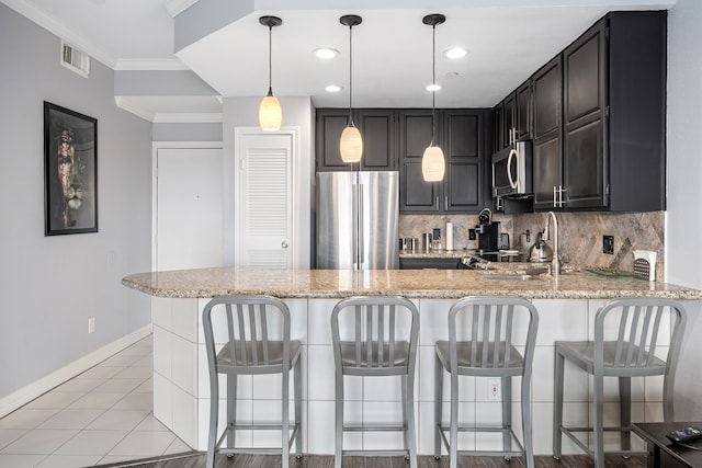 kitchen with light tile patterned floors, ornamental molding, appliances with stainless steel finishes, light stone counters, and kitchen peninsula