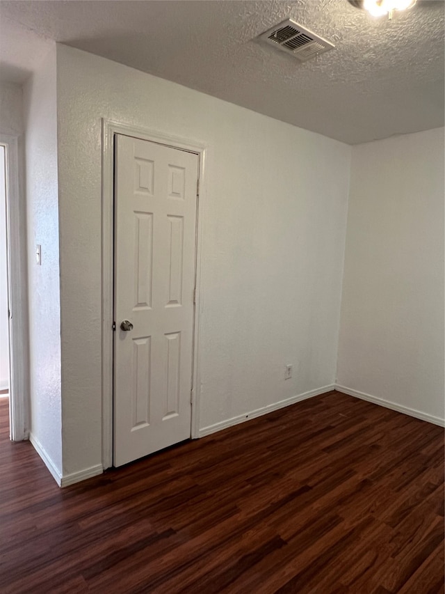 spare room featuring a textured ceiling and dark hardwood / wood-style flooring