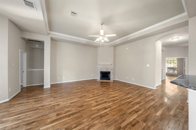 unfurnished living room featuring a tiled fireplace, wood-type flooring, ornamental molding, and ceiling fan