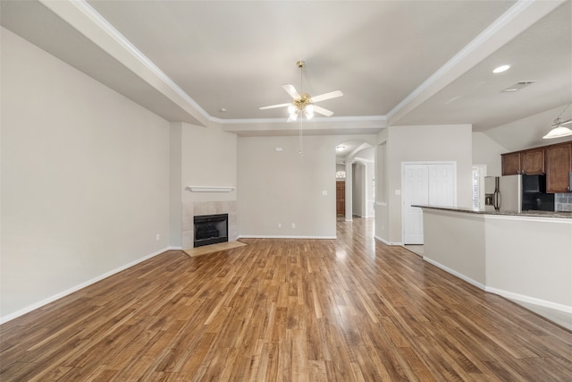 unfurnished living room featuring hardwood / wood-style floors, a tiled fireplace, and ceiling fan