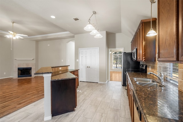 kitchen featuring hanging light fixtures, a tile fireplace, dark stone countertops, sink, and light wood-type flooring