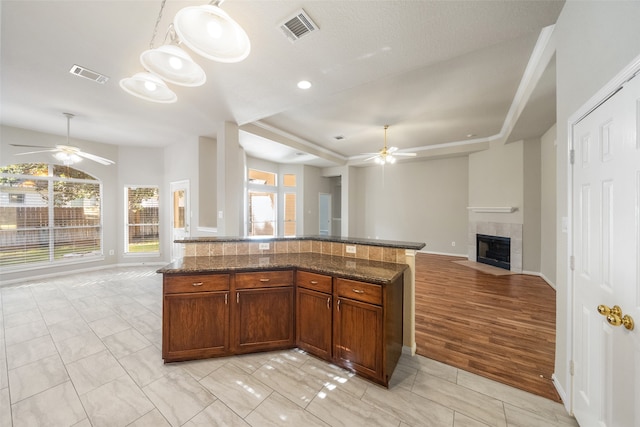 kitchen featuring a tile fireplace, light hardwood / wood-style flooring, a healthy amount of sunlight, and dark stone counters