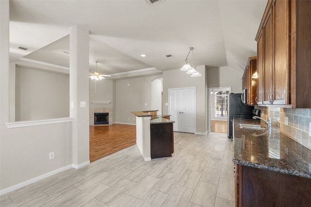 kitchen with tasteful backsplash, sink, light hardwood / wood-style floors, ceiling fan, and dark stone countertops