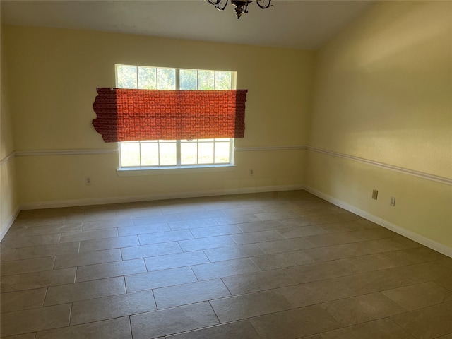 tiled empty room featuring an inviting chandelier