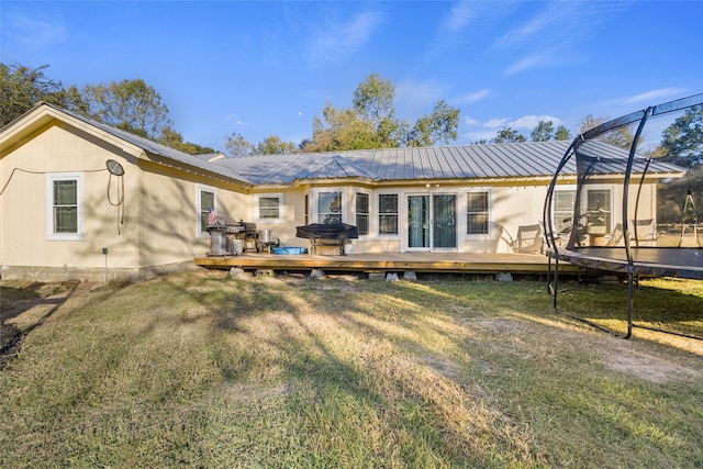 rear view of property featuring a deck, a yard, and a trampoline