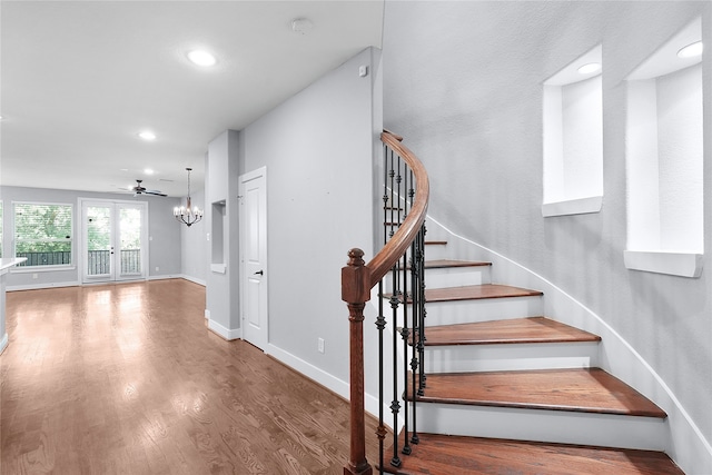 stairs with french doors, ceiling fan with notable chandelier, and hardwood / wood-style flooring