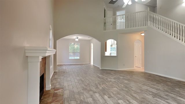 unfurnished living room featuring ceiling fan, hardwood / wood-style flooring, a high ceiling, and a tile fireplace