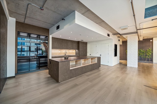 kitchen with sink, dark brown cabinets, light wood-type flooring, and a kitchen island