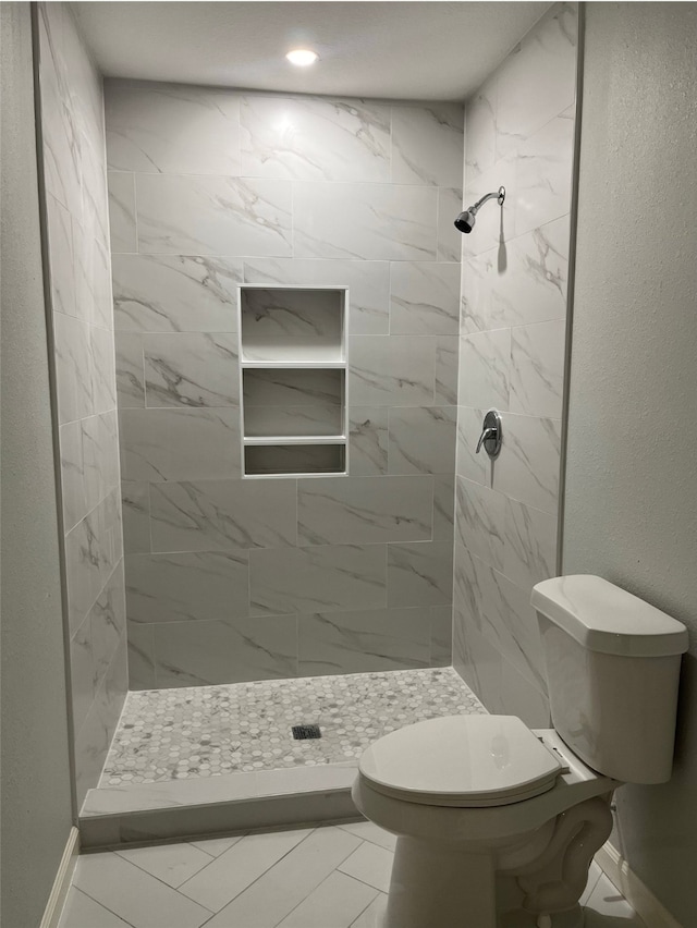 bathroom with tile patterned flooring, tiled shower, and toilet