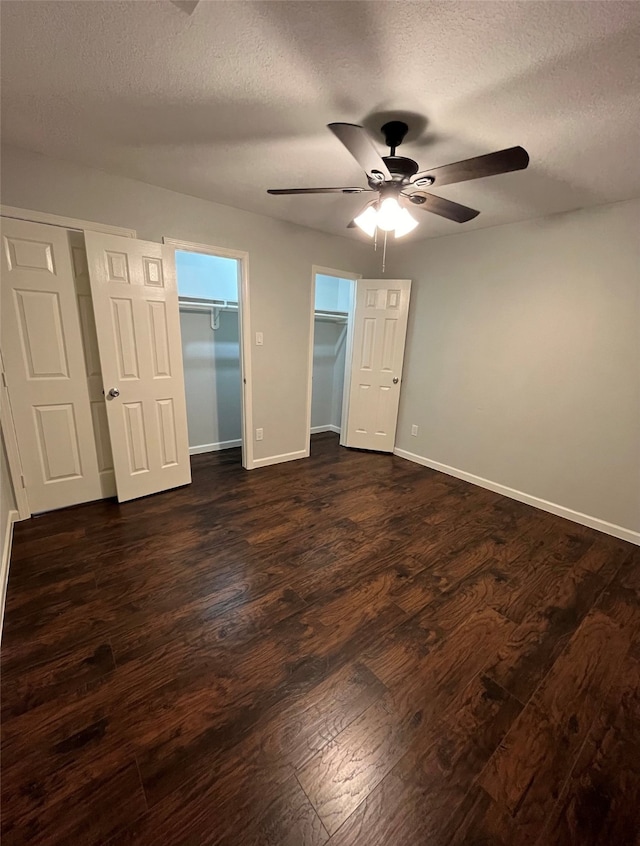 unfurnished bedroom featuring a spacious closet, a textured ceiling, ceiling fan, and dark hardwood / wood-style floors