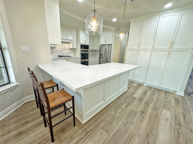 kitchen featuring white cabinets, tasteful backsplash, appliances with stainless steel finishes, light hardwood / wood-style flooring, and pendant lighting