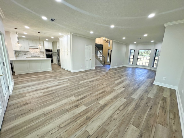 unfurnished living room featuring light hardwood / wood-style floors, crown molding, a textured ceiling, and an inviting chandelier