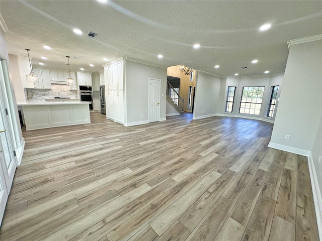 623 Barkaloo Rd, Baytown, TX 77521 - unfurnished living room with visible vents, crown molding, a notable chandelier, light wood-style floors, and stairs