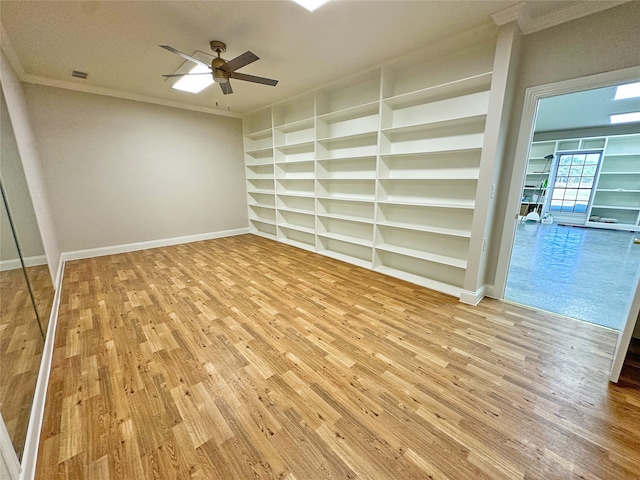 spare room with crown molding, light hardwood / wood-style flooring, built in shelves, and ceiling fan