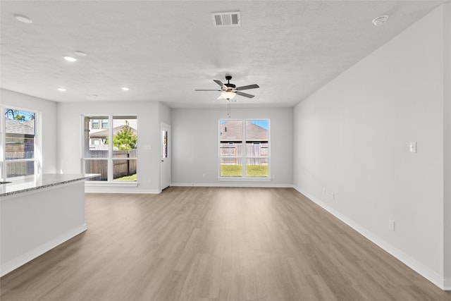 unfurnished living room featuring ceiling fan, a healthy amount of sunlight, light wood-type flooring, and a textured ceiling