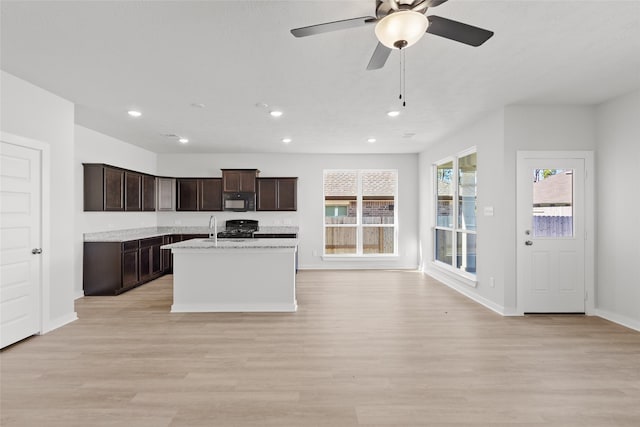 kitchen featuring light stone countertops, sink, an island with sink, black appliances, and light wood-type flooring