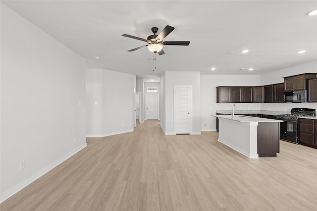 kitchen with dark brown cabinetry, ceiling fan, light hardwood / wood-style flooring, a kitchen island with sink, and black appliances