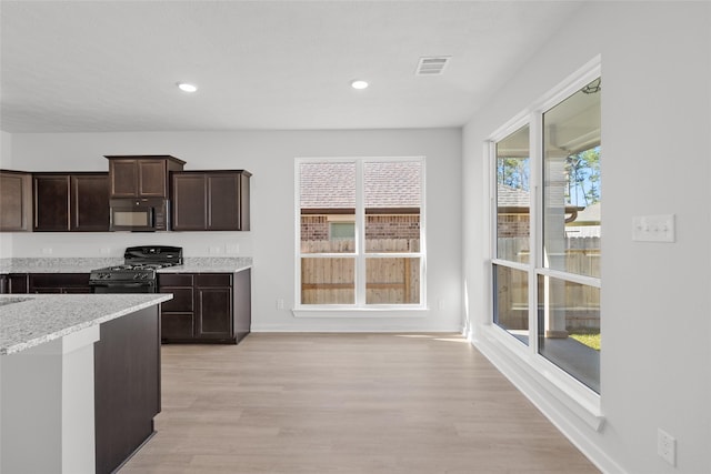 kitchen with dark brown cabinetry, plenty of natural light, black appliances, and light hardwood / wood-style flooring