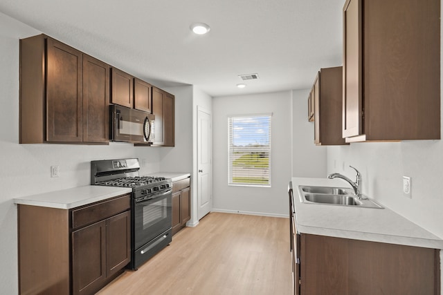 kitchen with dark brown cabinets, black appliances, sink, and light wood-type flooring