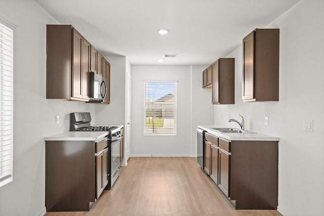 kitchen with sink, appliances with stainless steel finishes, dark brown cabinets, and light hardwood / wood-style floors