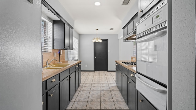 kitchen with sink, stainless steel gas cooktop, decorative light fixtures, wooden counters, and a chandelier