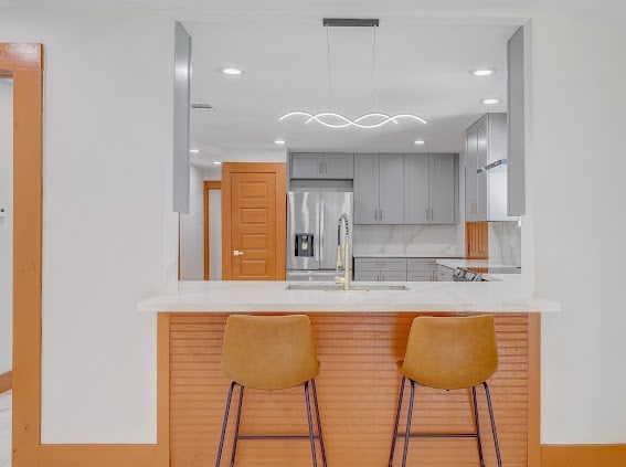 kitchen with a breakfast bar area, gray cabinetry, tasteful backsplash, and stainless steel fridge with ice dispenser