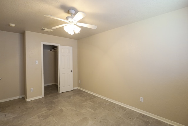 unfurnished bedroom featuring a walk in closet, a textured ceiling, a closet, and ceiling fan