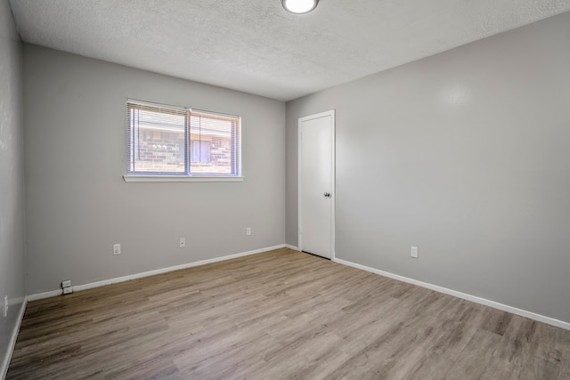 empty room with a textured ceiling and light hardwood / wood-style flooring