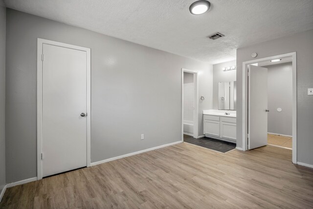 unfurnished bedroom featuring light hardwood / wood-style floors, connected bathroom, and a textured ceiling