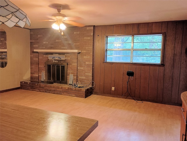 unfurnished living room with light hardwood / wood-style flooring, wood walls, ceiling fan, and a brick fireplace