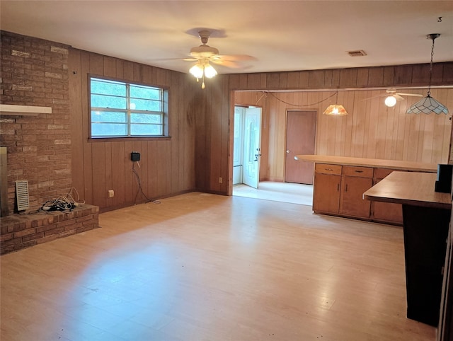 unfurnished living room with light hardwood / wood-style flooring, wood walls, and ceiling fan