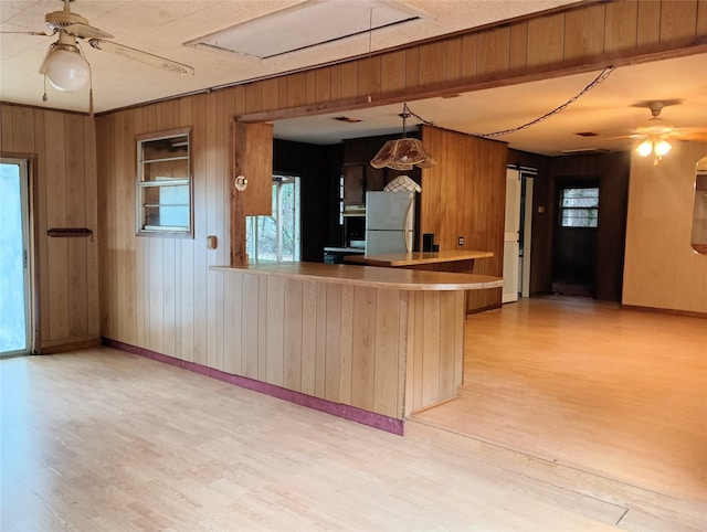 kitchen with stainless steel fridge, wooden walls, kitchen peninsula, and light hardwood / wood-style floors