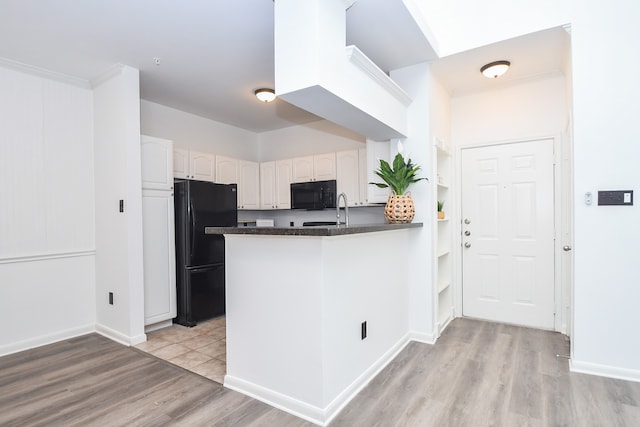 kitchen with light hardwood / wood-style floors, white cabinetry, sink, black appliances, and kitchen peninsula