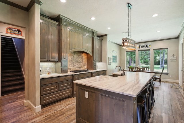 kitchen with pendant lighting, a center island with sink, dark hardwood / wood-style floors, light stone countertops, and gas cooktop